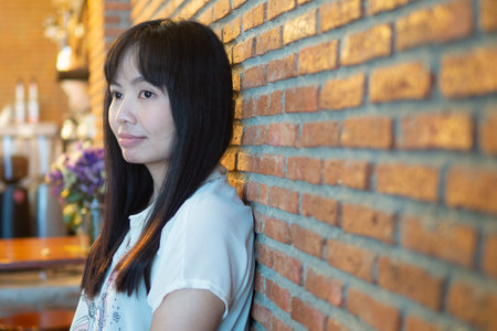 Young Asian woman leaning  the red brick block wall and smiling happily.の写真素材