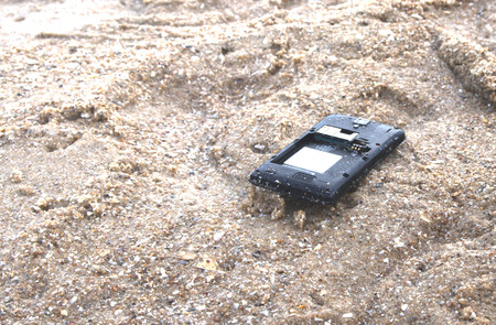 Close up of broken mobile phone drop on sea beach with copy space, High Contrast, Shallow Depth of Fieldの写真素材