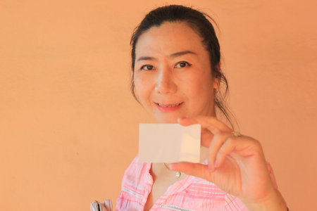 Young asian woman showing a blank business card on an orange backgroundの写真素材