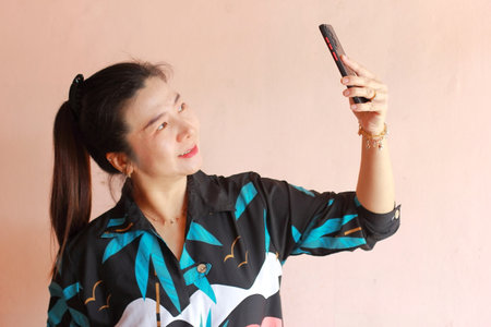 Asian woman take a selfie with mobile phone on pink wall background.の写真素材