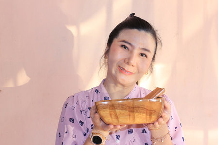 Asian woman holding a wooden bowl with bamboo spoon in the morning.の写真素材