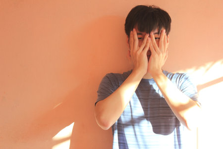 Asian young man is sad and covering his face with his hands.の写真素材
