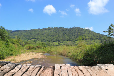 Wooden bridge over the river or stream with blue sky and green mountain background, woodden table.の写真素材