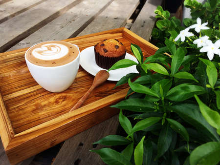 Latte coffee and Banana Chocolate cup cake on the wooden tray in the gardenの写真素材