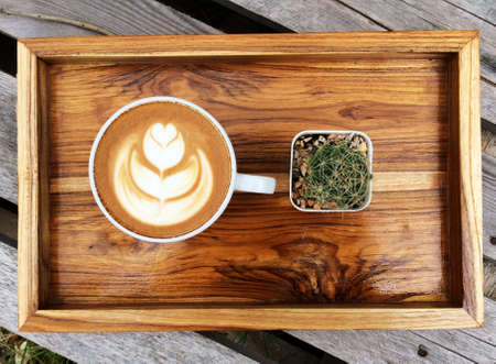 Latte art coffee in White cup and Cactus on the wooden tray,Coffee cup on gardenの写真素材