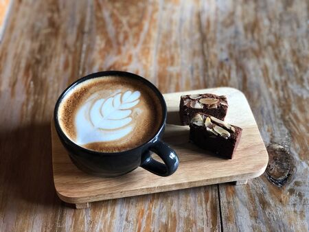 Top view Delicious Breakfast;  Latte art coffee in Black cup and Brownie topped with almond sliced in wooden tray on the vintage wooden table.の写真素材