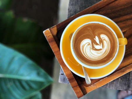 top view of  heart shape latte art coffee in yellow and white cup on the vintage wooden table with  green garden background . Love coffee love in your cup.の写真素材