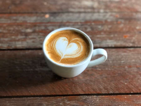 heart love piccolo latte  in white cup on wooden table with  natural light , vintage style and copy space. piccolo coffee with heart latte art on rustic wood tableの写真素材