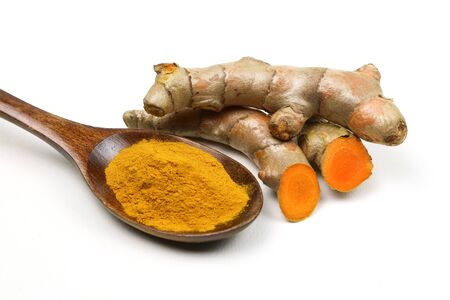 Turmeric powder in a wooden spoon and fresh turmeric roots isolated on a white background is an ingredient in turmeric foods and ingredients in skin care products. Turmeric helps strengthen the skin.の写真素材