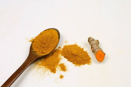 Turmeric powder in a wooden spoon and fresh turmeric roots isolated on a white background is an ingredient in turmeric foods and ingredients in skin care products. Turmeric helps strengthen the skin.の写真素材