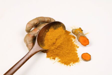 Turmeric powder in a wooden spoon and fresh turmeric roots isolated on a white background is an ingredient in turmeric foods and ingredients in skin care products. Turmeric helps the skin to be strong.の写真素材