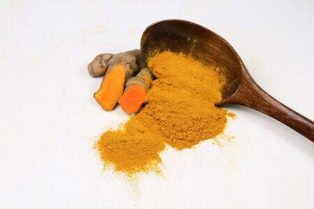 Turmeric powder in a wooden spoon and fresh turmeric roots isolated on a white background is an...
