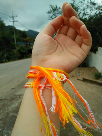 <p>Hand with orange and yellow bracelets on a background of the road. The ceremony to tie holy thread on wrist.</p>の写真素材