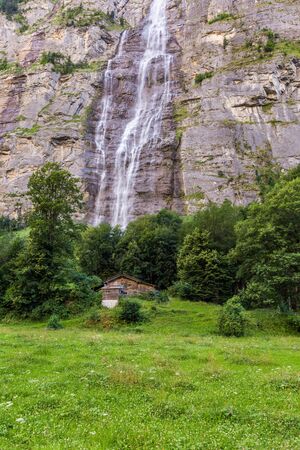 Waterfall and small house in Jungfrau valley in Lauterbrunnen, Switzerlandの写真素材