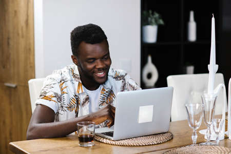 A young African American man sits in a room and communicates via video communication with friends....