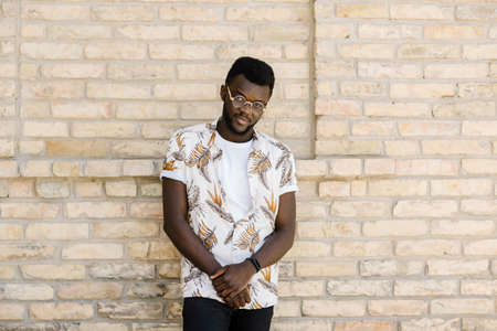 Happy African American man in sunglasses stands near a brick building on the street on a sunny day. Close-up portraitの写真素材