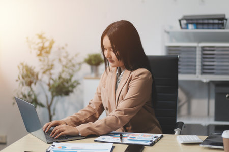 Asian Businesswoman Using laptop computer and working at office with calculator document on desk, doing planning analyzing the financial report, business plan investment, finance analysis concept.の写真素材