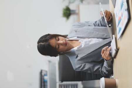 Successful Asian businesswoman smiling using laptop computer and holding coffee cup at office. Confident Asia businesswoman sitting happily in the office.の写真素材
