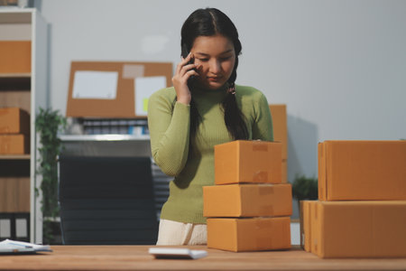 Startup SME small business entrepreneur of freelance Asian woman wearing apron using laptop and box to receive and review orders online to prepare to pack sell to customers, online sme business ideas.の写真素材