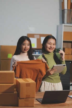 Startup SME small business entrepreneur of freelance Asian woman wearing apron using laptop and box to receive and review orders online to prepare to pack sell to customers, online sme business ideas.の写真素材