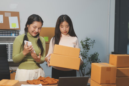 Startup SME small business entrepreneur of freelance Asian woman wearing apron using laptop and box to receive and review orders online to prepare to pack sell to customers, online sme business ideas.の写真素材