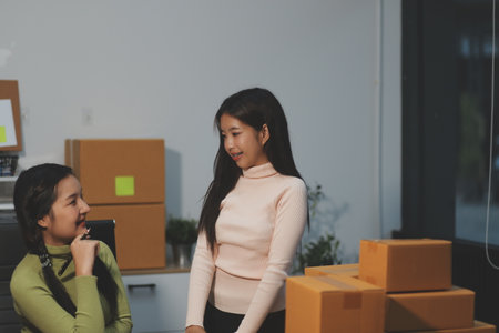 Startup SME small business entrepreneur of freelance Asian woman wearing apron using laptop and box to receive and review orders online to prepare to pack sell to customers, online sme business ideas.の写真素材
