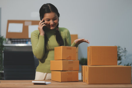 Startup SME small business entrepreneur of freelance Asian woman wearing apron using laptop and box to receive and review orders online to prepare to pack sell to customers, online sme business ideas.の写真素材
