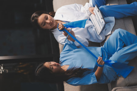 Doctor physiotherapist assisting a patient while giving exercising treatment on stretching his arm with exercise band in the clinic, Rehabilitation physiotherapy conceptの写真素材