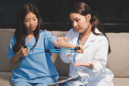 Physiotherapist assisting a patient while giving exercising treatment on stretching her arm with exercise band in the clinic, Rehabilitation physiotherapy conceptの写真素材