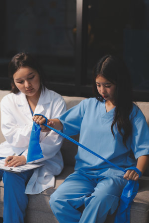 Doctor physiotherapist assisting a patient while giving exercising treatment on stretching his arm with exercise band in the clinic, Rehabilitation physiotherapy conceptの写真素材