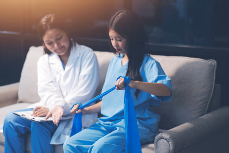 Physical therapist assisting a patient while giving exercising treatment on stretching her arm with exercise band in the clinic, Rehabilitation physiotherapy conceptの写真素材