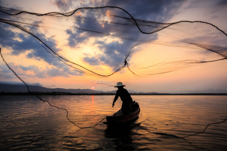 Silhouetted of a fisherman in the morning on the lakeの写真素材