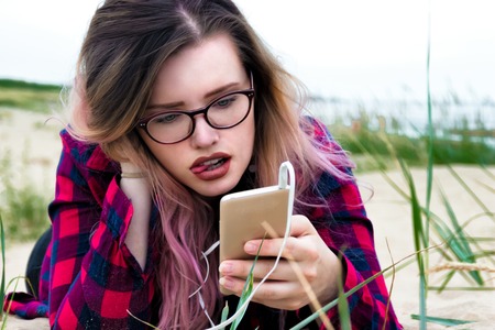 Fashion portrait of young hipster women with beautiful smile using smartphone. Summer concept, sandy...