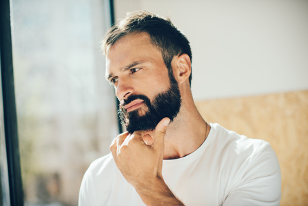 Portrait of a handsome bearded man wering white tshirt and thinking about somethingの写真素材