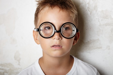 Cute little boy with glasses smiling on the white wall backgroundの写真素材