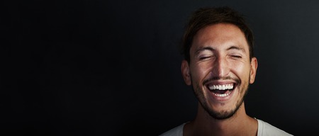 Portrait of cute young man wearing white tshirt and laughing  a lot. Black backgroundの写真素材