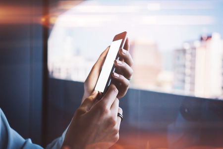 A girl holding a smartphone in her hand. Sunlight effects on the screen. Blurred backgroundの写真素材