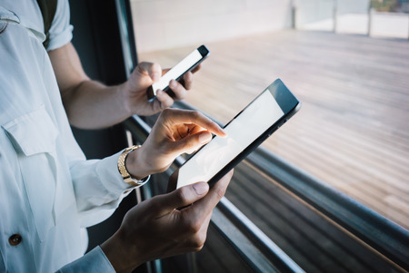 Guy and a girl holding in hands their gadgets. They both touching the screen. They showing something on the screen. Blurred background.の写真素材
