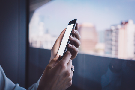 Smartphone holding in female hand on the blured city backgroundの写真素材