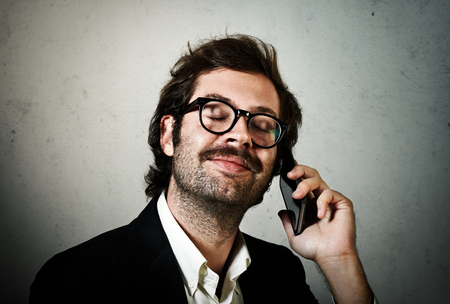 Stylish young man wearing trendy suit and talking with smartphone. Concrete wall on the background.の写真素材