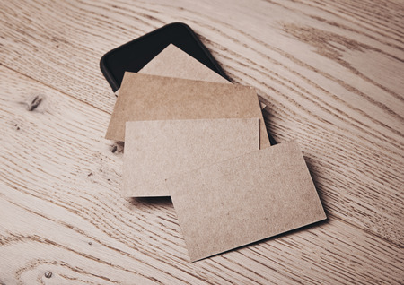 Close up of blank and craft business cards on natural wood table. Generic design smart phone under the business cards. Horizontalの写真素材