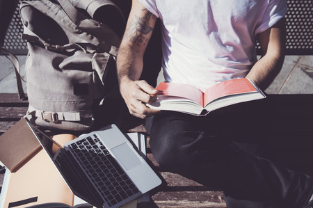 Closeup photo man waring white tshirt sitting city park and reading book. Studying at the...