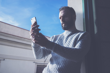 Photo bearded man making selfie mobile phone. Man using contemporary smartphone, blue sky background, sunny day.の写真素材