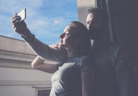 Young couple summer holiday city. Photo woman and bearded man making selfie smartphone in modern loft. Using contemporary smartphone. Horizontal, film effect.の写真素材
