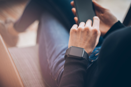 Closeup photo of female hands touching screen smartphone and wearing generic design smart watch. Film effects, blurredの写真素材