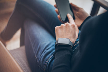 Photo of woman touching screen smartphone and wearing generic design smartwatch. Film effects, blurred background.の写真素材