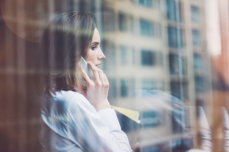 Young business woman wearing modern suit and talking smartphone and holding papers in hands. Open...