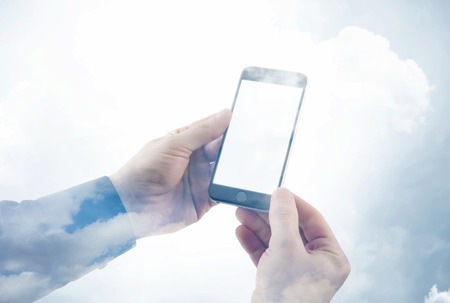 Double exposure photo businessman holding modern smartphone hands. Reflection of clouds background, white blank screen ready for your business information. Horizontalの写真素材