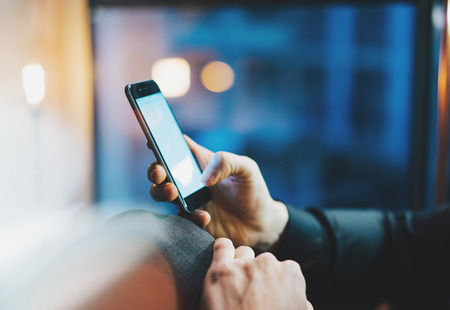 Closeup photo businessman relaxing on modern loft office. Man sitting in chair at night. Using contemporary smartphone, blurred background. Horizontalの写真素材