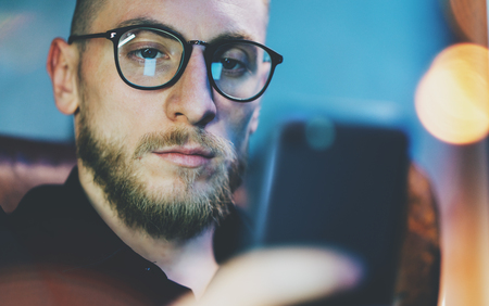 Photo bearded businessman relaxing modern loft office. Banker sitting in vintage chair, looking mobile phone. Using contemporary smartphone. Blurred background. Horizontalの写真素材